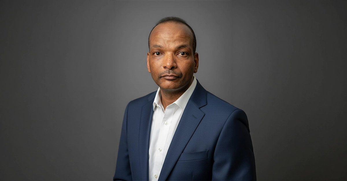 Professional headshot of a man in a navy suit against a dark grey background